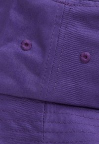 Gorra morada hecha de tejido texturizado, con costuras visibles y dos ojales bordados contrastantes para ventilación.