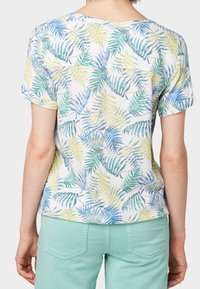Top de manga corta y ligero con un estampado multicolor de hojas en amarillo, verde y azul sobre un fondo blanco.