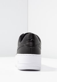Black leather sneaker viewed from the back with a white thick sole and a logo on the heel tab against a white background.