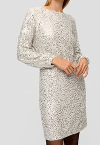 Paljettklänning i ljus silver med lös passform, rund halsringning och långa ärmar. Har en texturerad yta med reflekterande paljetter och manschettärmar.