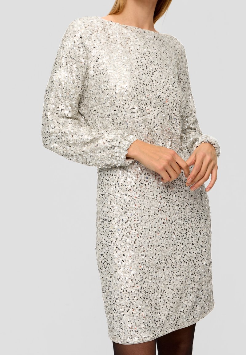 Paljettklänning i ljus silver med lös passform, rund halsringning och långa ärmar. Har en texturerad yta med reflekterande paljetter och manschettärmar.