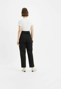 Pantaloni neri a vita alta con un taglio dritto, dettagli con tasche posteriori, abbinati a una semplice t-shirt bianca e scarpe di colore chiaro.
