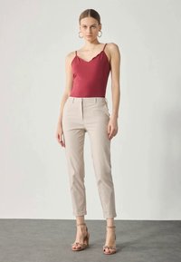 Rød tettsittende tank topp med tynne stropper, kombinert med lyse beige skreddersydde bukser og nude sandaler med en knute-detalj. Glatt stoff, minimalistisk design.
