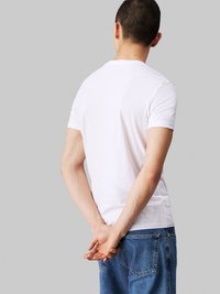 White cotton t-shirt with short sleeves and a round neckline, worn with blue denim jeans, viewed from the back. Smooth texture.