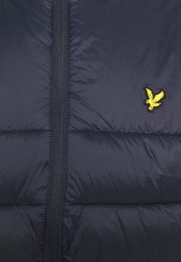 Granatowa kurtka puchowa z pionowym zamkiem i charakterystycznym żółtym haftowanym logo ptaka. Posiada pikowane sekcje dla izolacji i faktury.