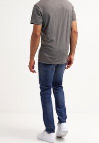 Grå bomullströja och blå denimjeans, kombinerat med vita sneakers. T-shirten har en enkel design med en etikett på baksidan.