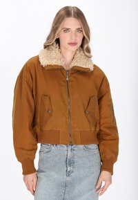 Giacca marrone cropped con colletto foderato in pelliccia, chiusura con zip, due tasche frontali, polsini a coste e tessuto testurizzato.