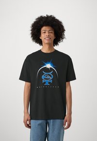 Čierne bavlnené tričko so stredným modrým grafickým dizajnom a slovom "QUIKSILVER" dole, v kombinácii s svetlomodrými džínsy.