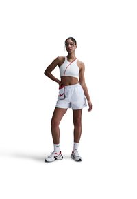 Un reggiseno sportivo bianco e pantaloni corti bianchi, abbinati a scarpe da ginnastica con accenti rossi, dotati di una borsa grigia e rossa con il logo Nike sul corpo.
