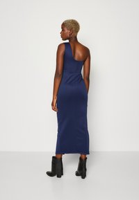 Robe midi ajustée bleu marine avec une conception asymétrique à une épaule, texture lisse et fermeture éclair au dos. Des bottines noires s'accordent parfaitement avec le look.