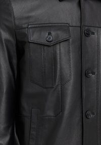 Zwarte leren jas met een kraag, sluiting met knopen aan de voorkant en twee borstzakken. Geverfde textuur met zichtbare stiksels.