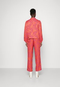Ensemble de veste et pantalon à motifs roses avec des designs tourbillonnants, des manches longues bouffantes et un pantalon large taille haute. Talons blocs blancs.