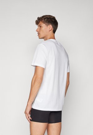 Vit bomullströja med korta ärmar, rund hatt och en avslappnad passform, bärs med svarta shorts. Slät textur, minimalistisk design.