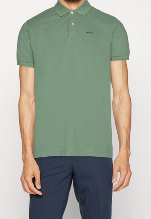 Man wearing a green short-sleeve polo shirt with a collar and two buttons, paired with dark blue pants.