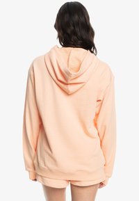 Hoodie v broskyňovej farbe s textúrovaným vnútorným podšívaním, dlhými rukávmi a kapucňou. Zadná časť má voľný strih a rebrovaný spodný lem.