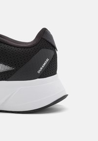 Scarpa da corsa nera con tomaia in rete, controfferta prominente, intersuola bianca e dettagli neri testurizzati. È visibile il nome del modello "Duramosl".