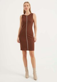 Braun gestreiftes Midi-Kleid mit ärmellosem Design, Frontreißverschluss und silbernen Details. Kombiniert mit beigefarbenen knielangen spitzen Stiefeln.