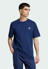 Tamsiai mėlynas medvilninis marškinėliai trumpomis rankovėmis ir apvalia iškirpte, su baltu Adidas logotipu ant krūtinės. Prigludusi, bet atsipalaidavusi dizaino linija.