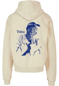 Felpa crema con una grande grafica blu di una persona che si copre il viso, con il testo "Tupac." Tessuto morbido, vestibilità comoda e cappuccio con cordino.
