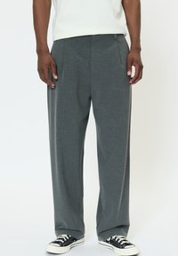 Sivé na mieru šité nohavice v úzkom strihu s záhybmi a hladkou textúrou, kombinované s čiernymi plátenými teniskami s bielymi šnúrkami.