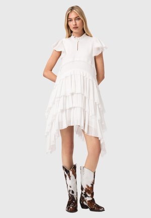 Biała, warstwowa sukienka z falbaniastymi rękawami, dekoltem z wycięciem i nierównym dołem. Do tego brązowo-białe kowbojskie botki z wzorem.