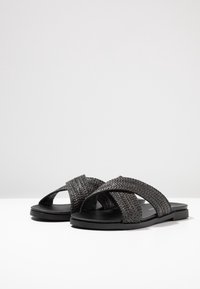 Svarta vävda sandaler med korsade remmar, platt sula och slät yta. Tillverkade av hållbara material och med en minimalistisk design.