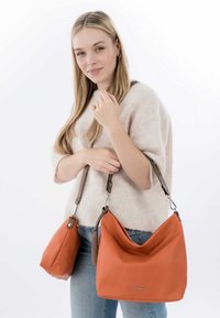 Orangefarbene Leder-Schultertasche mit lässigem Design und braunem Tragegurt, begleitet von einer kleineren passenden Tasche. Glatte Textur, minimalistische Details.