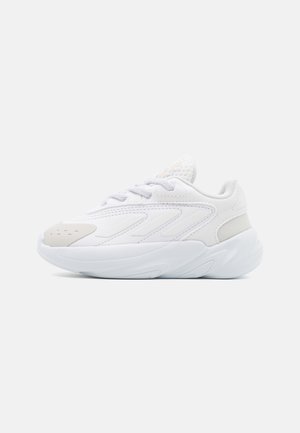 Biały sportowy sneaker z grubą podeszwą, siateczkowym językiem i sznurowanym fasonem, pokazany z boku na jednolitym tle.
