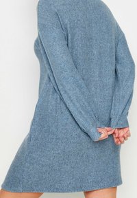 Robe en laine bleu clair avec des manches longues, une coupe décontractée et une longueur au genou. Texture subtile visible sur la surface du tissu.