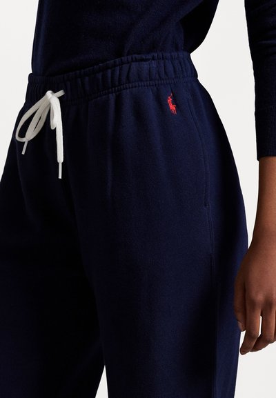Navy Sweatpants aus weichem Stoff; verfügen über einen elastischen Bund mit weißem Kordelzug und einem kleinen roten Logo-Akzent an der Seite.