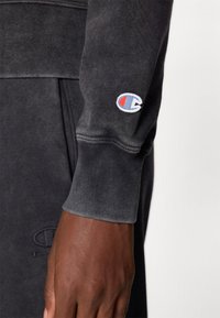 Manica di felpa grigia e testurizzata con polsino a coste. Presenta un piccolo logo ricamato in rosso, bianco e blu sul braccio.