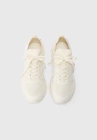 Une paire de baskets de sport blanc cassé avec des lacets noués en nœuds, vue de dessus sur un fond blanc uni.