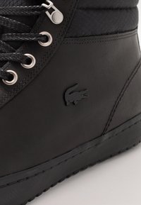 Czarny wysokogatunkowy sneaker wykonany ze skóry z teksturowaną tkaniną, z srebrnymi przelotkami, czarnymi sznurówkami i subtelnym logo krokodyla.