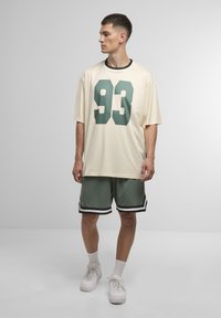 Fløjlstrik med grønntal "93," parret med grønne shorts med sort og hvid striber. En afslappet pasform øger komforten.