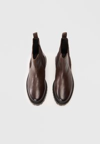 Bottines en cuir marron avec des côtés élastiques, des bouts arrondis et des semelles en caoutchouc texturées. Équipées d'une languette pour un enfilage facile.