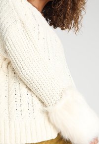 Pull crème en maille torsadée à manches longues ; doté de poignets en fausse fourrure blanche douce et d'un ourlet côtelé. Motif texturé sur tout le tissu.