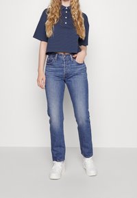 Camiseta polo corta a rayas marinas con mangas cortas, jeans de tiro alto azules y zapatillas blancas. Botones simples y textura clásica de denim.