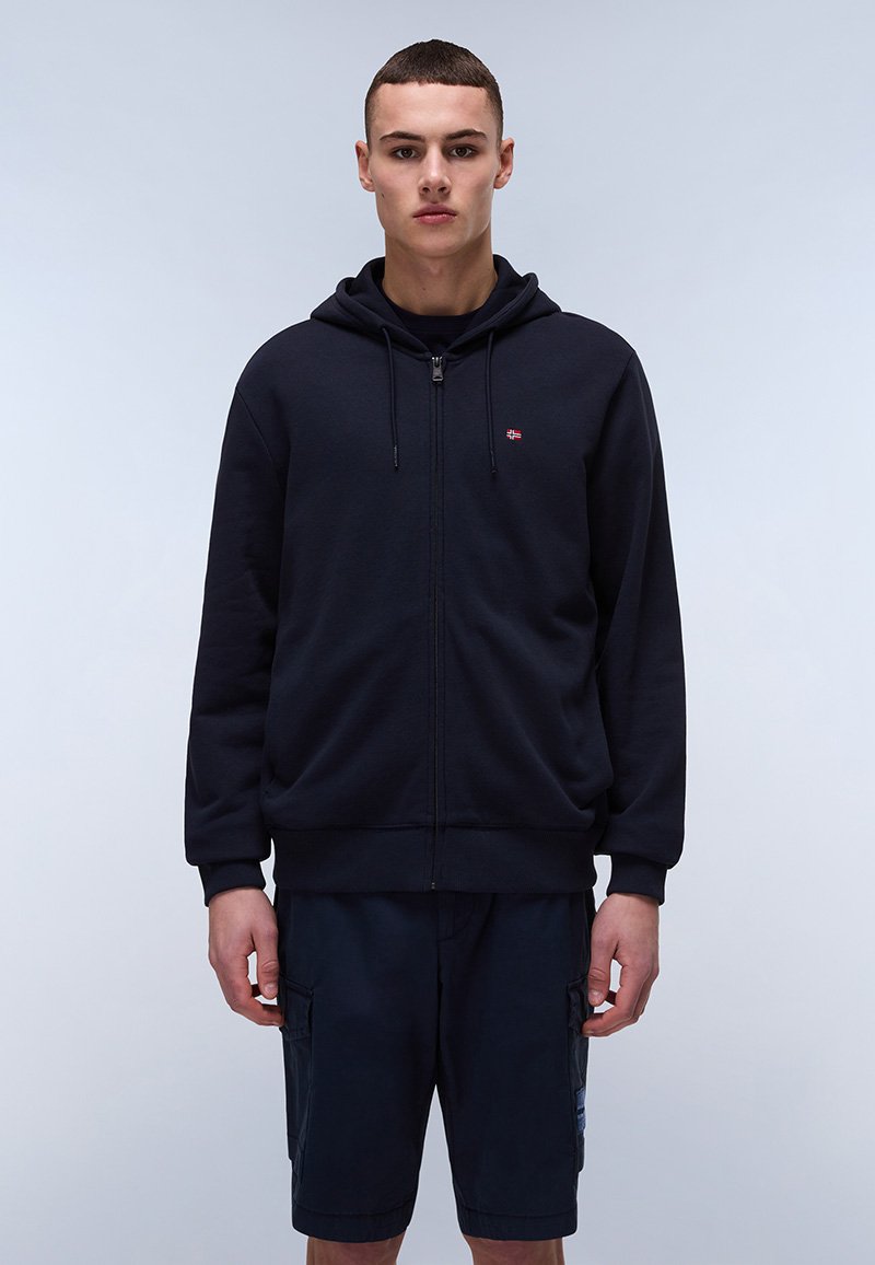 Felpa con zip di colore blu scuro, dotata di tasca a marsupio, cappuccio con cordini e piccolo logo sul petto. Abbinata a pantaloni corti blu navy con tasche cargo.