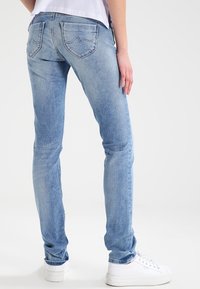 Modré džíny skinny s lehkým praním, s prošívaným designem zadní kapsy. Spárováno s bílými teniskami, s mid-rise střihem.