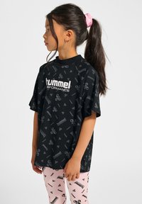 Svart kortärmad T-shirt med logotryck på hela plagget och texten "hummel PERFORMANCE". Rundad halsringning, avslappnad passform och mjukt tyg.