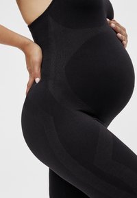 Leggings de maternidad negras con un diseño texturizado y un acabado suave, que destacan una forma ajustada que se adapta a una barriga en crecimiento.