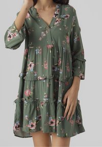 Robe verte à fleurs avec un col en V, manches longues et volants à étages. Présente diverses fleurs colorées et un tissu doux et léger.