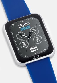 Slimwatch met een vierkant gezicht, zwart display, zilveren bezel en blauwe siliconen band. Bevat verschillende wijzerplaten en een datumindicator.