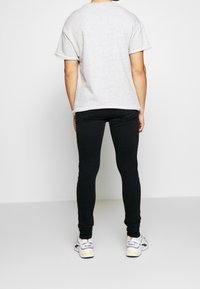 Camiseta gris de gran tamaño con mangas enrolladas, combinada con jeans ajustados negros y zapatillas deportivas blancas con detalles en amarillo.