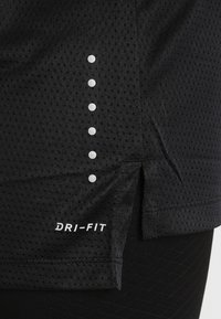 Tela atlética negra y transpirable con seis puntos reflectantes alineados verticalmente y "DRI-FIT" impreso cerca del dobladillo, con detalle de abertura lateral.