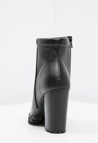 Bottine en cuir noir avec un talon aigu haut, fermeture éclair sur le côté, et finition texturée, mettant en valeur un matériau lisse et durable.