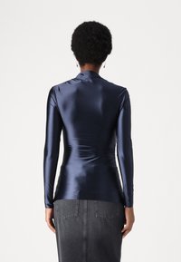 Mørkeblå satin bluse med lange ærmer, der har en tætsiddende pasform og let rynkning på ryggen, parret med en grå denimskørt.
