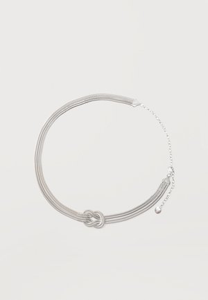 Collier en chaîne multibrins argenté avec un détail central en forme de nœud et une extension de fermoir réglable sur un fond clair uni.