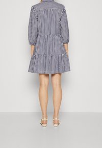 Robe rayée à volant, en bleu marine et blanc. Elle présente des manches longues et un col, fabriquée en tissu léger.