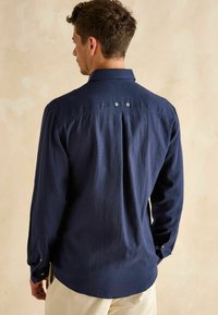 Námornícky modrá košela s dlhým rukávom a golierom na gombíky, s dvoma ventilačnými otvormi na chrbte a gombíkovými manžetami, vyrobená z textúrovanej látky.